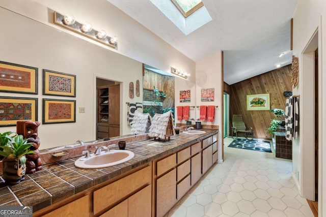 bathroom featuring wooden walls, double vanity, a skylight, and a sink