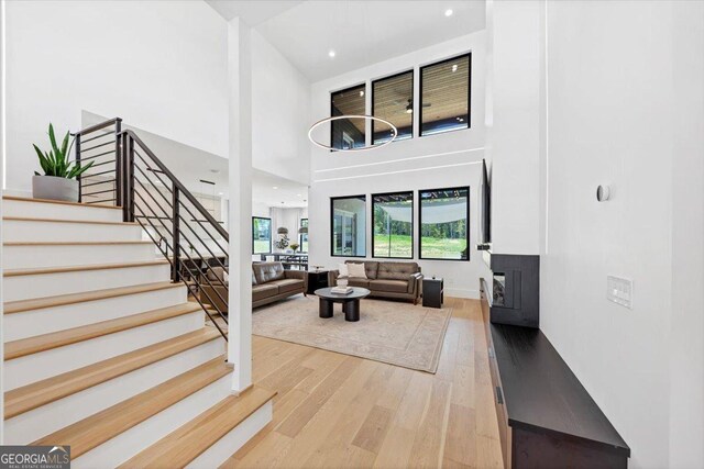living room featuring stairs, light wood-style floors, a high ceiling, and a fireplace