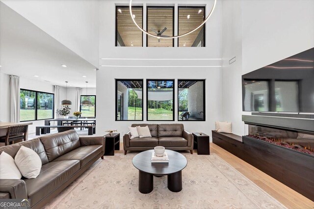 living area featuring a glass covered fireplace, wood finished floors, and a towering ceiling