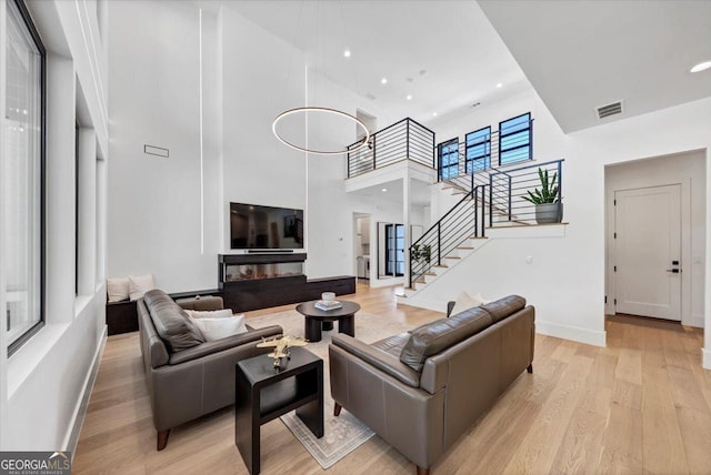 living room featuring stairs, a high ceiling, light wood-style flooring, baseboards, and visible vents