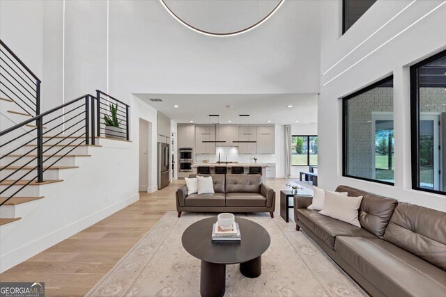 living area with light wood finished floors, baseboards, a towering ceiling, visible vents, and stairway
