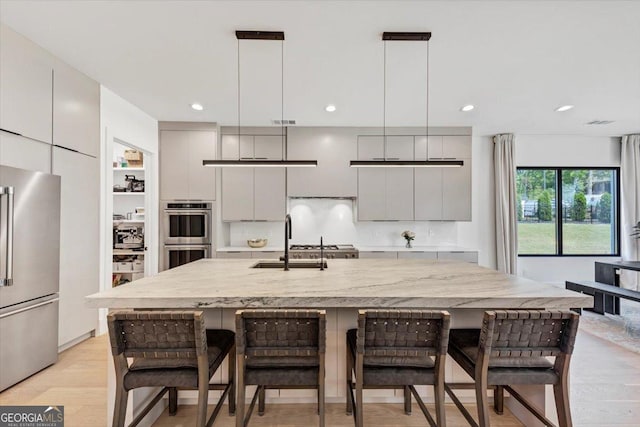 kitchen featuring stainless steel appliances, a sink, modern cabinets, a kitchen bar, and hanging light fixtures