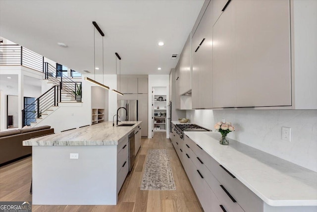 kitchen featuring light wood-style flooring, a sink, a spacious island, modern cabinets, and pendant lighting