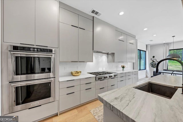 kitchen featuring a sink, light wood-type flooring, stainless steel appliances, gray cabinetry, and recessed lighting