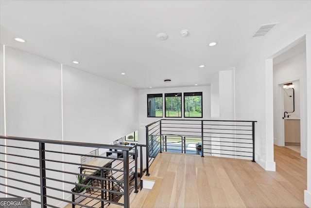 hallway featuring recessed lighting, wood finished floors, visible vents, an upstairs landing, and baseboards