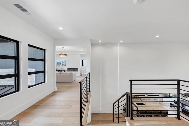 corridor featuring an upstairs landing, light wood finished floors, baseboards, visible vents, and recessed lighting