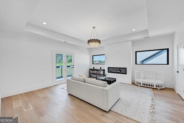 living area featuring a tray ceiling, light wood-type flooring, baseboards, and recessed lighting
