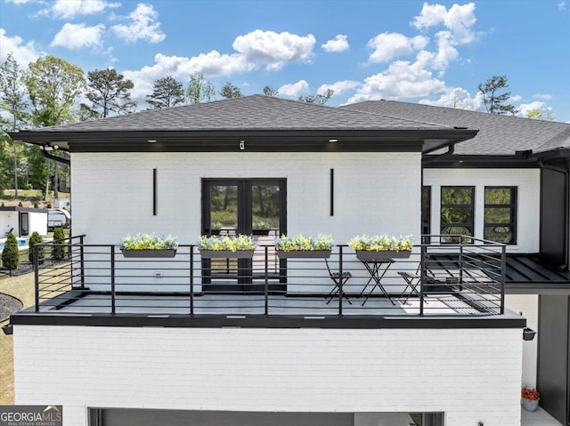back of property featuring brick siding, french doors, roof with shingles, and a balcony