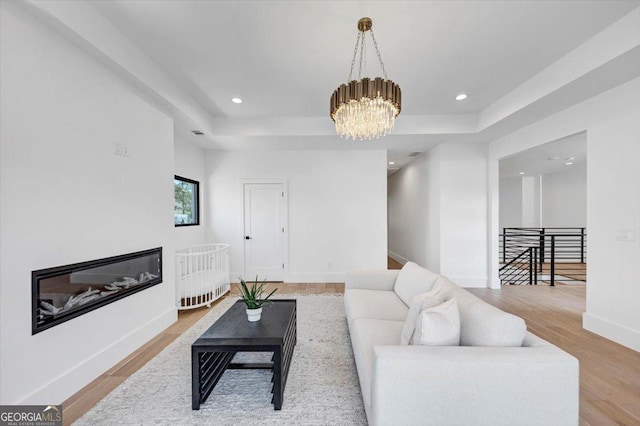 living area with wood finished floors, an inviting chandelier, a tray ceiling, baseboards, and recessed lighting