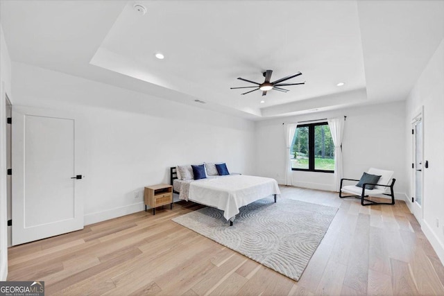 bedroom with baseboards, recessed lighting, light wood-style flooring, and a raised ceiling