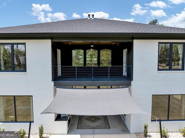 back of property with a shingled roof, a balcony, and brick siding