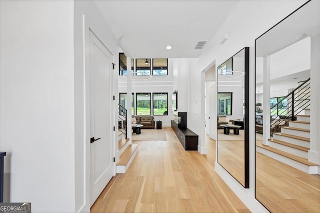 corridor with light wood-style floors, stairway, visible vents, and baseboards