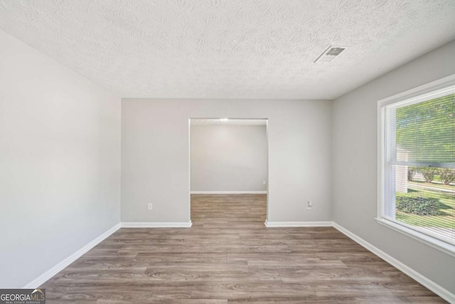 unfurnished room with wood finished floors, visible vents, a textured ceiling, and a healthy amount of sunlight