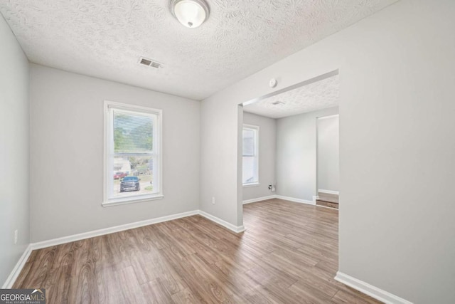 unfurnished room with visible vents, wood finished floors, a textured ceiling, and a healthy amount of sunlight