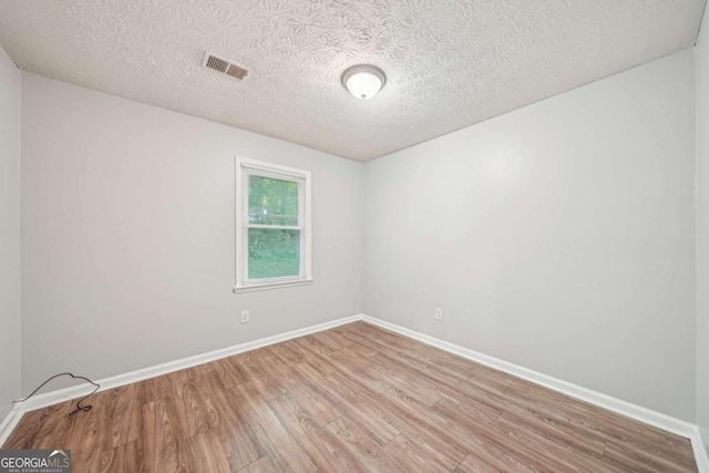 empty room featuring baseboards, wood finished floors, visible vents, and a textured ceiling