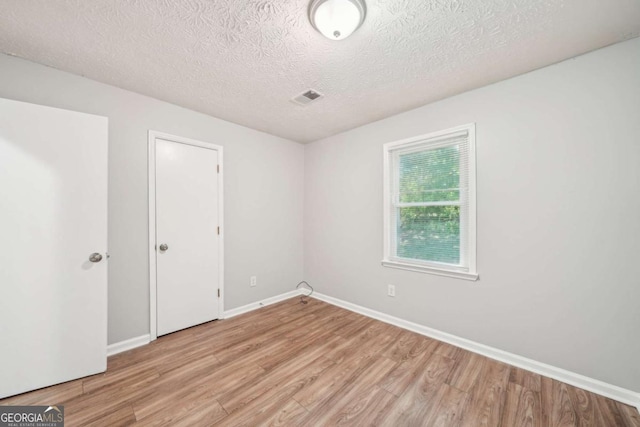empty room featuring light wood-style floors, baseboards, visible vents, and a textured ceiling