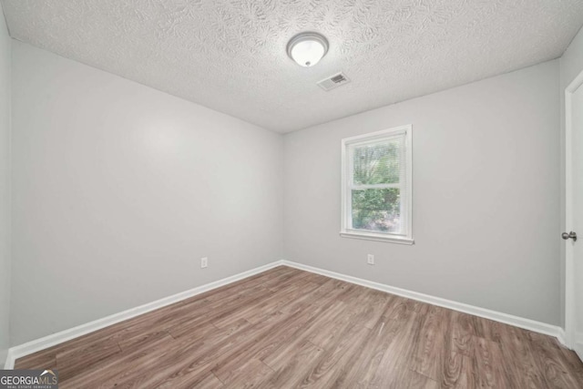 unfurnished room featuring wood finished floors, a textured ceiling, baseboards, and visible vents