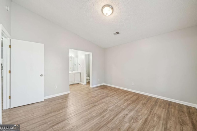 unfurnished bedroom with lofted ceiling, visible vents, light wood-style floors, baseboards, and a textured ceiling