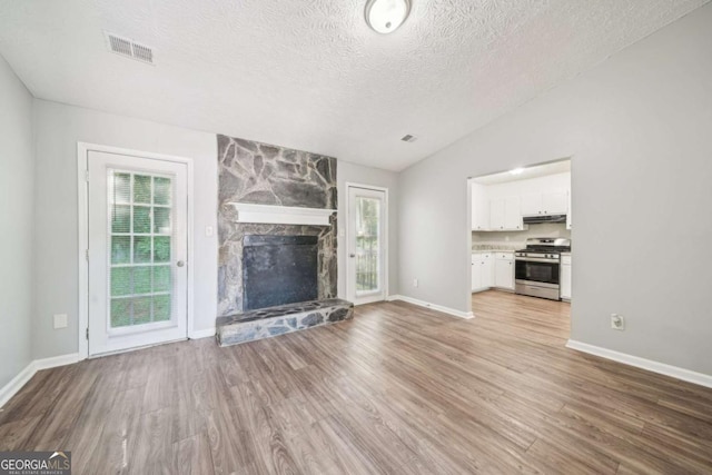 unfurnished living room featuring a stone fireplace, a textured ceiling, light wood finished floors, lofted ceiling, and visible vents