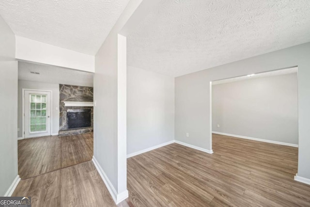 unfurnished living room with baseboards, a stone fireplace, wood finished floors, and a textured ceiling