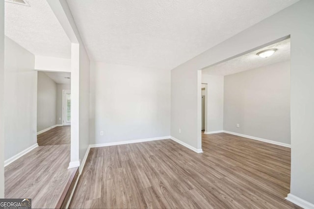 unfurnished living room featuring wood finished floors, a textured ceiling, and baseboards