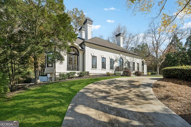 view of front of property featuring a chimney, a front lawn, a shingled roof, and stucco siding