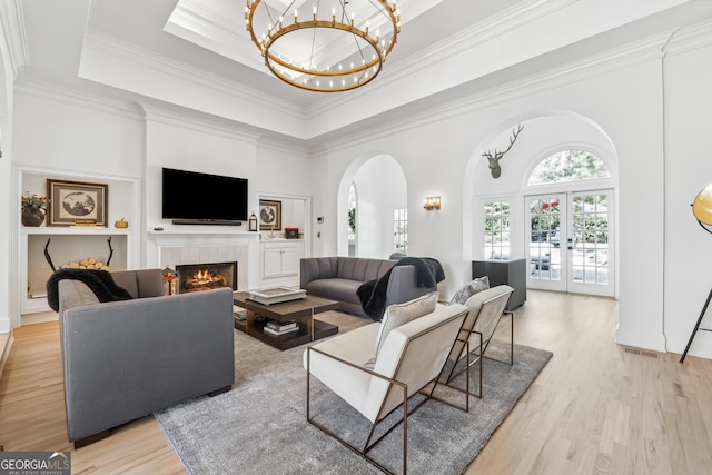 living area featuring a tile fireplace, a towering ceiling, an inviting chandelier, arched walkways, and light wood-style floors