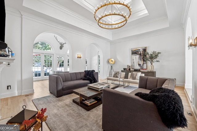 living room featuring a tray ceiling, ornamental molding, arched walkways, light wood-type flooring, and a notable chandelier