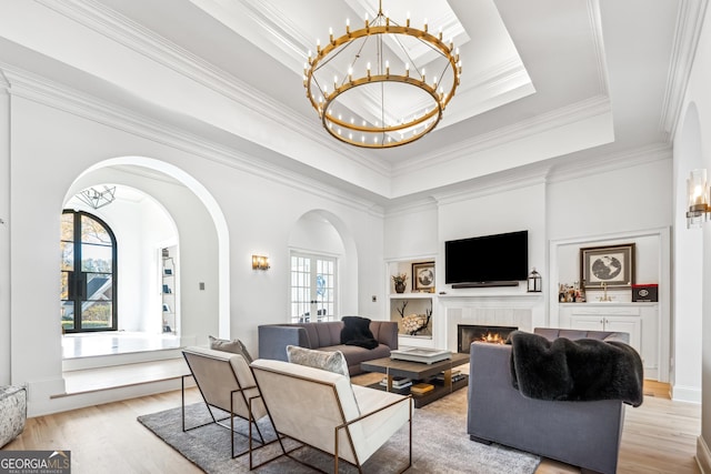 living room featuring a tile fireplace, light wood finished floors, ornamental molding, arched walkways, and a notable chandelier