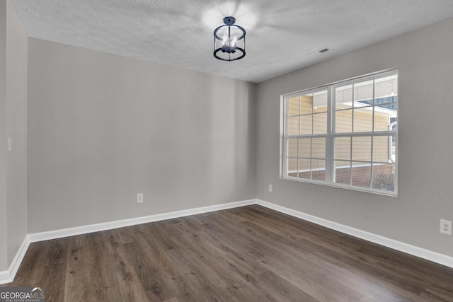 empty room with a chandelier, dark wood finished floors, visible vents, and baseboards