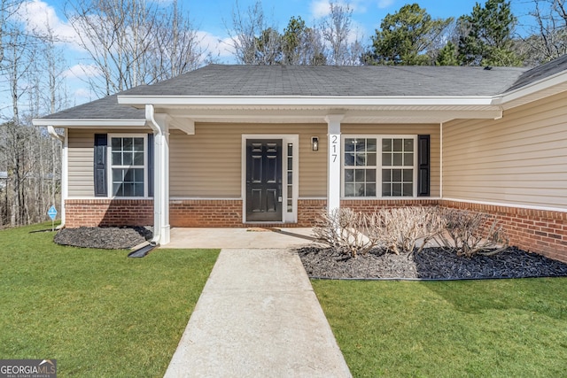 doorway to property with a lawn, brick siding, a porch, and roof with shingles