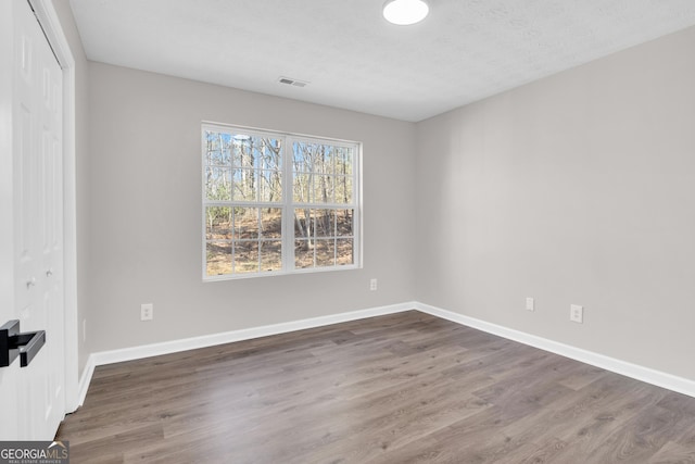 unfurnished room with baseboards, wood finished floors, and visible vents