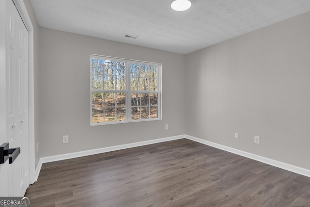 spare room featuring visible vents, baseboards, a textured ceiling, and dark wood finished floors