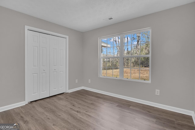 unfurnished bedroom featuring baseboards, wood finished floors, visible vents, and a closet