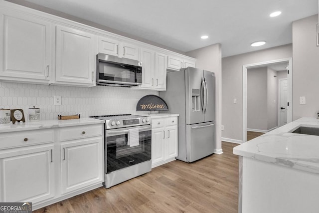 kitchen with decorative backsplash, stainless steel appliances, light wood-style flooring, white cabinetry, and light stone countertops