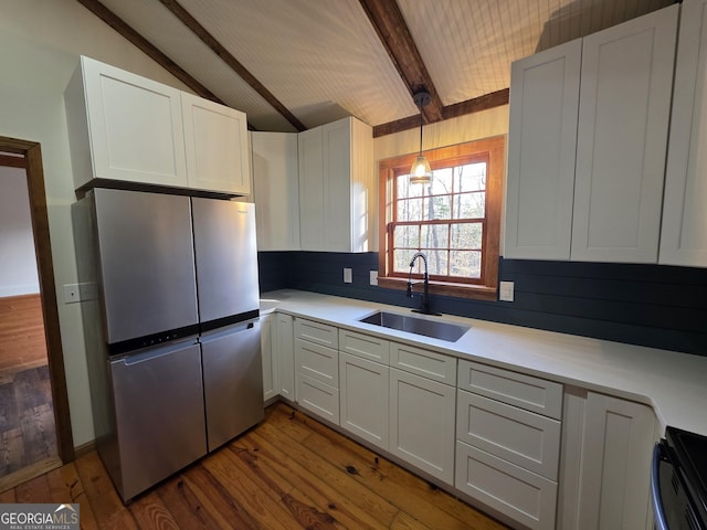 kitchen featuring a sink, lofted ceiling with beams, light countertops, dark wood-style floors, and freestanding refrigerator