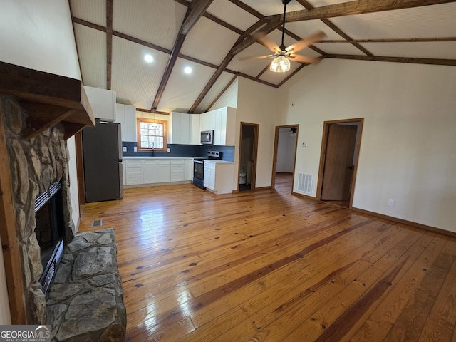 unfurnished living room with light wood finished floors, visible vents, a ceiling fan, beamed ceiling, and a fireplace