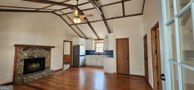 kitchen featuring a stone fireplace, a ceiling fan, freestanding refrigerator, high vaulted ceiling, and white cabinetry
