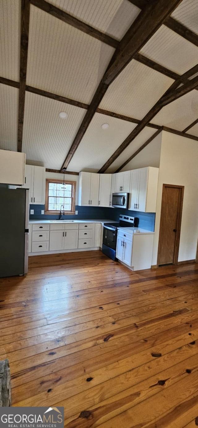kitchen with white cabinets, wood-type flooring, appliances with stainless steel finishes, and lofted ceiling with beams