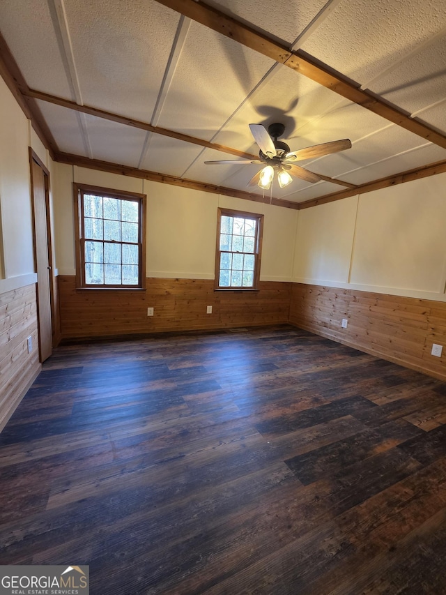 empty room with ceiling fan, a wainscoted wall, dark wood-type flooring, and wooden walls
