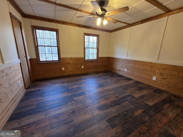 spare room featuring a wainscoted wall, wooden walls, dark wood-type flooring, and a ceiling fan