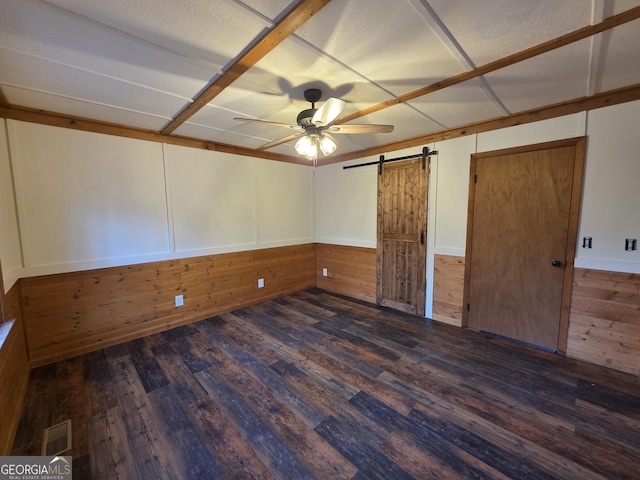 unfurnished bedroom with a barn door, wooden walls, wood finished floors, visible vents, and wainscoting