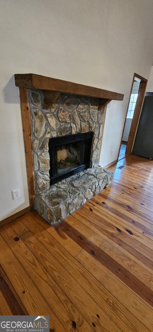 details featuring baseboards, wood finished floors, a stone fireplace, and refrigerator