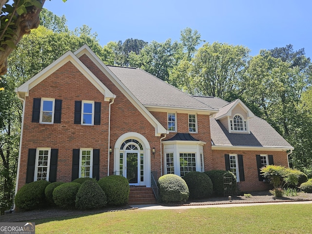 view of front of house featuring brick siding, roof with shingles, and a front lawn