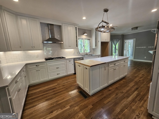 kitchen with dishwasher, wall chimney range hood, ornamental molding, a center island, and decorative backsplash