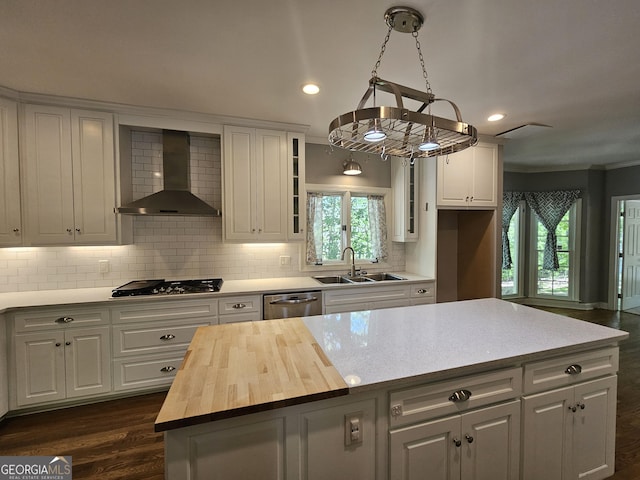 kitchen featuring stainless steel dishwasher, a sink, wood counters, gas cooktop, and wall chimney exhaust hood