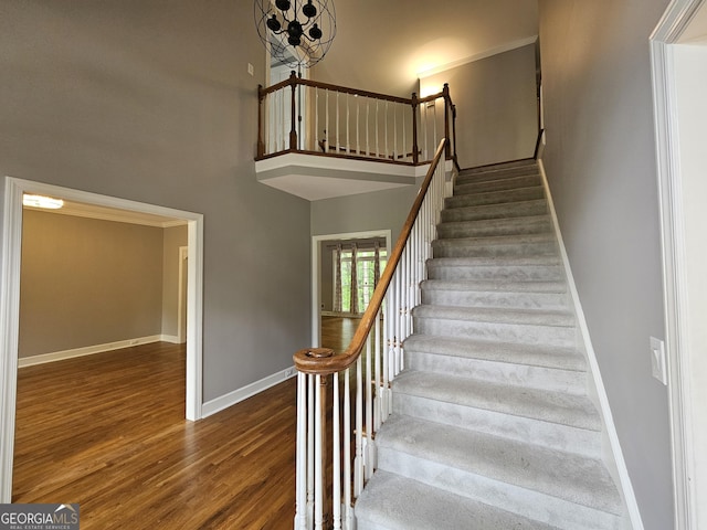 stairs featuring baseboards, wood finished floors, a towering ceiling, and a chandelier