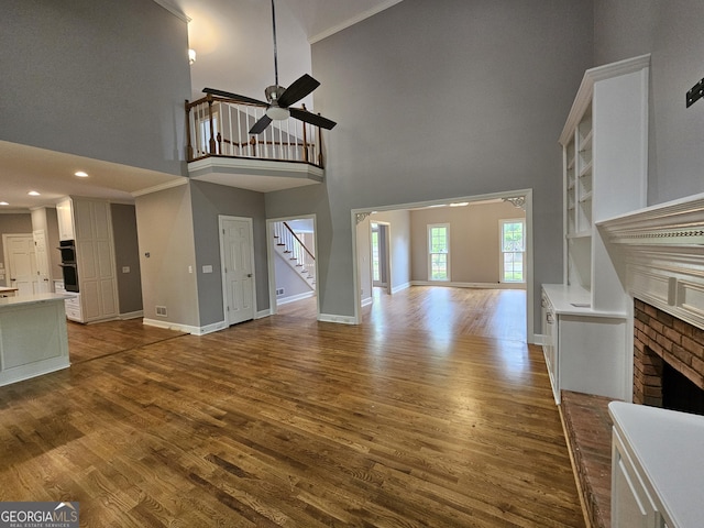unfurnished living room featuring baseboards, a towering ceiling, a ceiling fan, stairway, and a fireplace