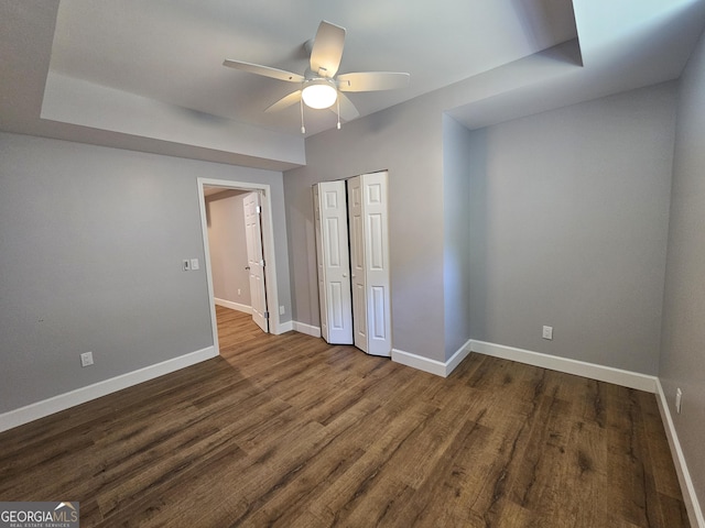 unfurnished bedroom with ceiling fan, a closet, baseboards, and dark wood-style flooring
