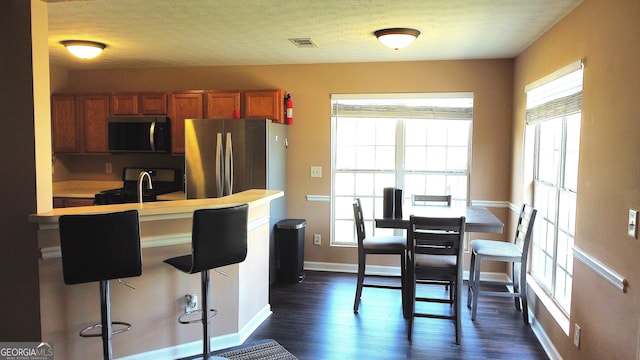 156 Roosevelt Blvd, Jackson, GA 30233 - kitchen with stainless steel appliances, dark wood-type flooring, baseboards, brown cabinetry, and a breakfast bar area